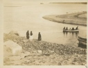 Image of People in small boat. Three women watching from shore